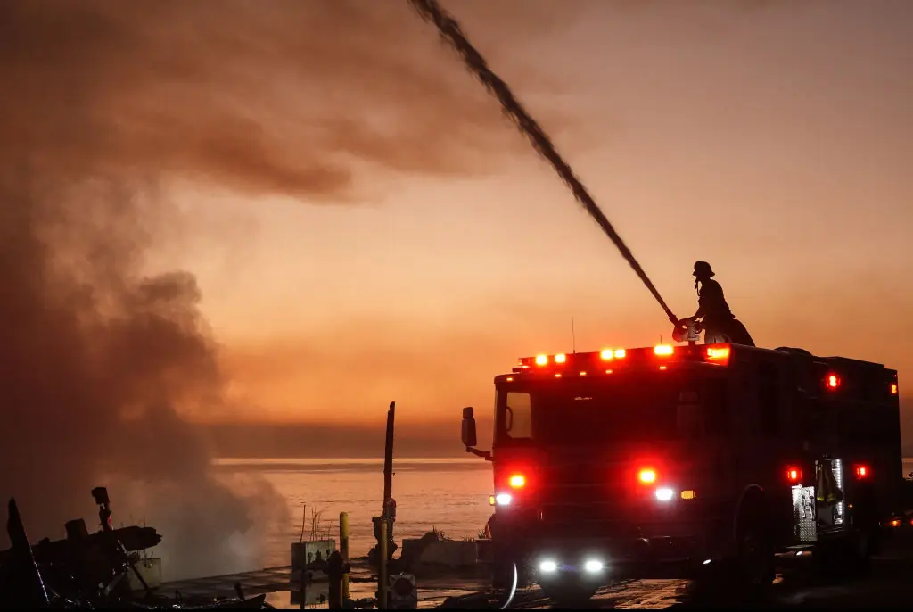 Firefighters spray water to combat flames at sunset in Pacific Palisades, California. Credit: NurPhoto / Getty