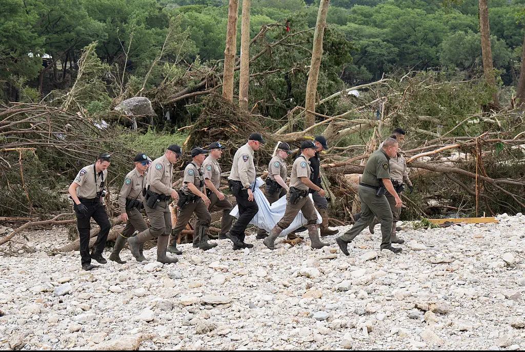 Texas Game Wardens and local law enforcement carry the body of a flood victim from the banks of the Guadalupe River during recovery operations. Credit: Eric Vryn / Getty