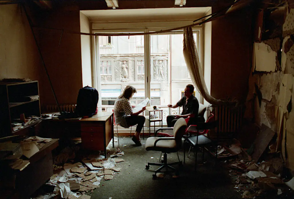 A Bosnian couple reads the newspaper in their bombed-out apartment along Marshal Tito Avenue in Sarajevo, 1992. Credit: David Turnley / Corbis / VCG / Getty Images.