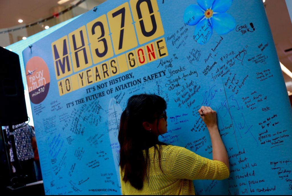 A woman signs a message of remembrance and hope on a MH370 memorial. 