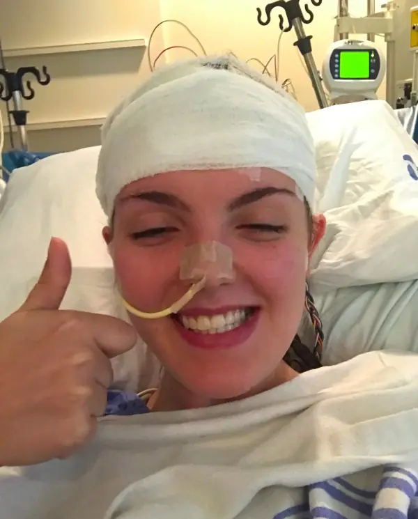 A woman smiling with a bandage around her head. 