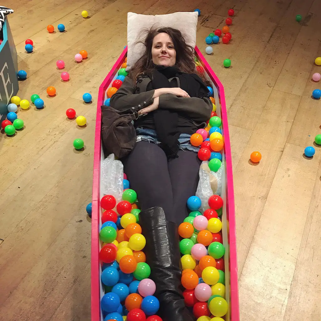 Erica Buist lying in a coffin filled with colored balls.