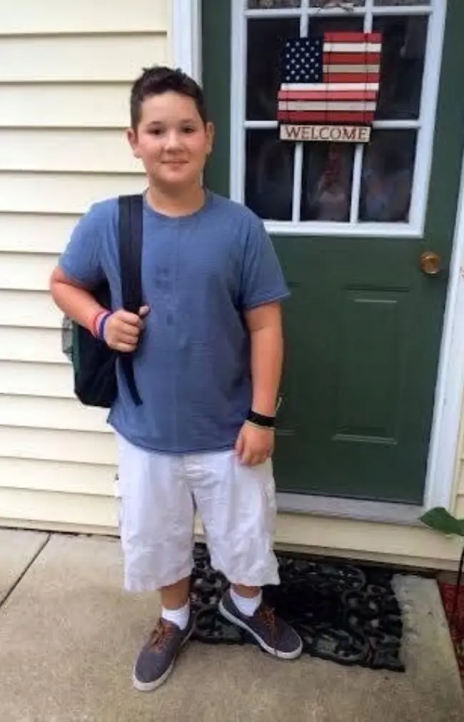 A boy standing outside his front door. 