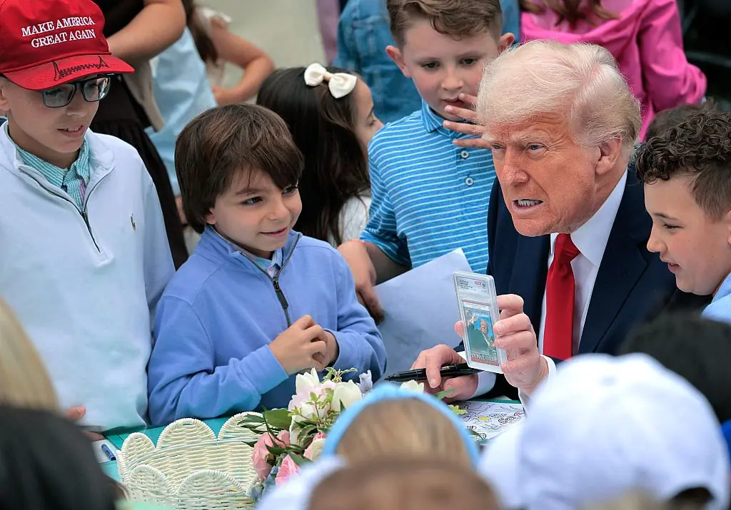 Trump shows a group of children a trading card of him raising a fist moments after surviving an attack on his life. Credit: Chip Somodevilla/Getty Imagesn 