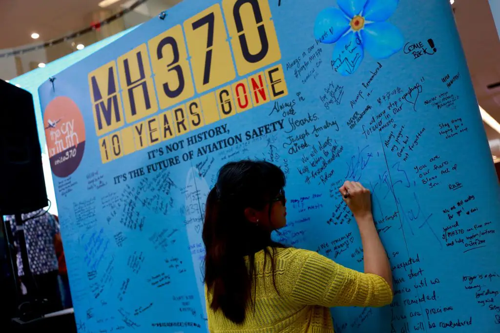 A woman signs a message of remembrance and hope on a MH370 memorial. Credit: NurPhoto/Getty