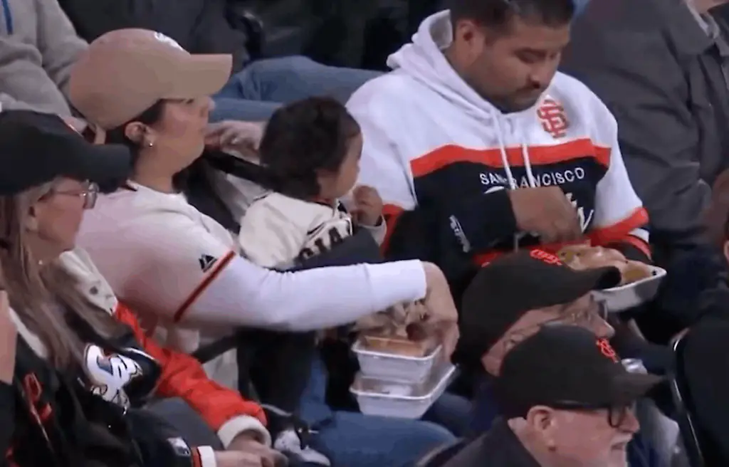 The man appeared to take one of the food boxes and begin eating while the woman continued holding the child and the remaining containers. Credit: NBC Sports